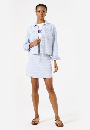 Lichtblauwe denimjacket en bijpassende rok met textuurpatroon. Bevat voorzakken en knoopsluiting op de jacket. Sandalen maken de look compleet.