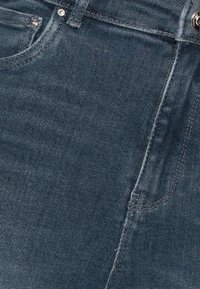 Tmavě modré džíny z denimu s klasickým pětikapsovým designem, robustním šitím a předním zapínáním na knoflík s kovovým akcentem.