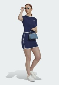 Mörkblå figursydd klänning med vit kant, kombinerad med vita sneakers och en liten blå strukturerad handväska. Moderiktiga solglasögon i retrostil.