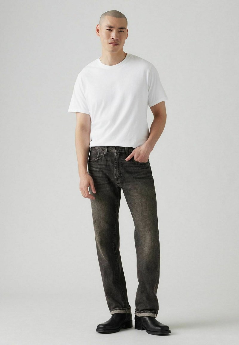 Witte katoenen t-shirt gecombineerd met donkergrijze denim jeans. Zwarte leren laarzen maken de outfit compleet, met een rechte pijp en subtiele slijtage.