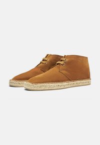 Botas de tobillo de ante marrón con diseño de cordones, que cuentan con una suela de cuerda de yute y una textura suave, puntera redondeada y detalles de costura mínimos.