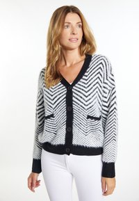 Schwarz-weiße Strickjacke mit Zickzackmuster, Knopfschluss, zwei Vordertaschen und gerippten Bündchen sowie Saum. Strukturierter Strickstoff.