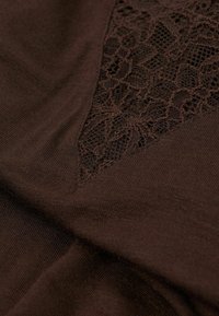 Brun tyg med en texturerad spetspanel. Slät yta på det mesta, intrikat spetsdetalj i triangelform på ena sidan.