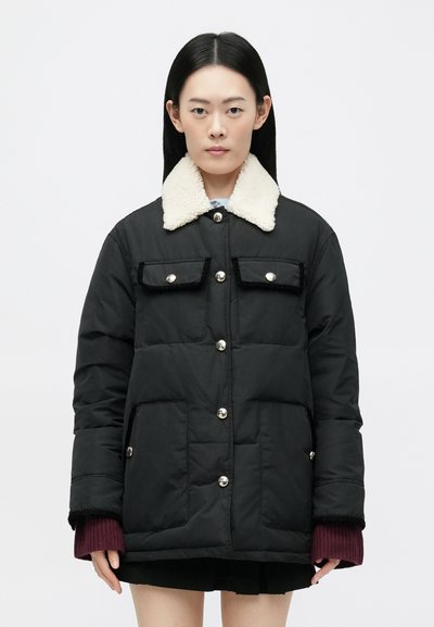 Black padded jacket with a white shearling collar, two front pockets, and silver hardware. Features a zip and button closure, ribbed cuffs.