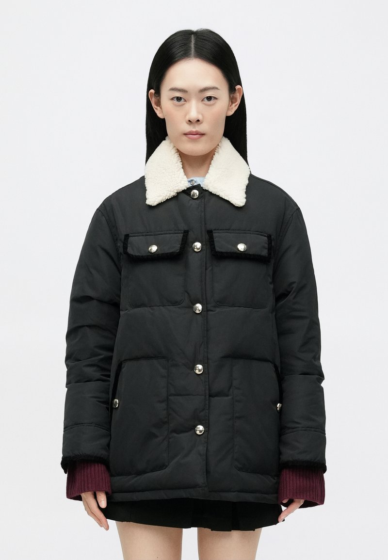 Sort polstret jakke med en hvid shearling krave, to forlommer og sølvfarvet hardware. Har lynlås- og knaplukning samt ribbede manchetter.