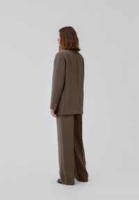 Bruin op maat gemaakt kostuum met een gestructureerde blazer met een enkele split en brede broekspijpen, gemaakt van een zachte, gestructureerde stof.