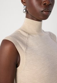 Bežna brezrokavna majica z visokim ovratnikom, izdelana iz mehkega materiala, z rebrastimi robovi in prilagojenim krojem. Dopolnjena z velikimi kovinskimi uhani.