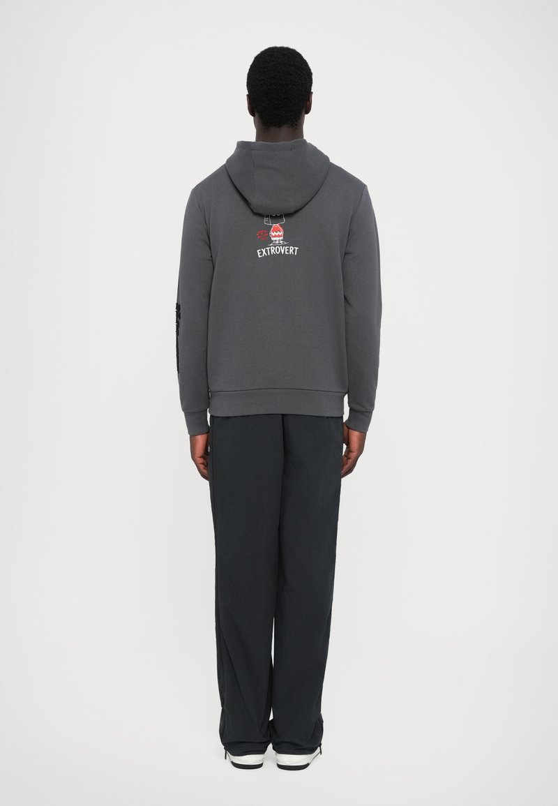 Gray hoodie with a back graphic reading "EXTROVERT," paired with loose black pants and white sneakers. Features a hood and long sleeves.