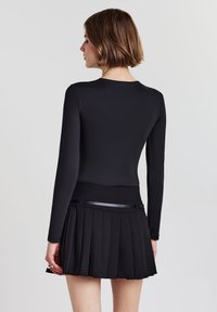 Maglietta nera a maniche lunghe con scollatura a girocollo abbinata a una gonna nera plissettata con una vita decorativa e una superficie texturizzata.
