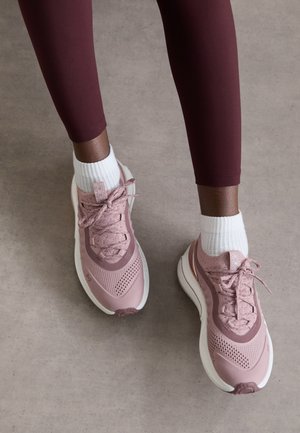 Scarpe sportive rosa chiaro con tomaia in rete testurizzata, chiusura con lacci e suola bianca. Indossate con calzini bianchi a tubino, abbinate a leggings bordeaux.