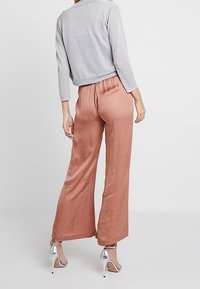 Ljust grå, långärmad topp med metallisk lyster, ihop med vida satinbyxor i rostfärg och silverfärgade högklackade sandaler.