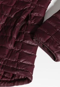 Giacca trapuntata borgogna con texture liscia, dotata di polsini elasticizzati, una tasca laterale e un design leggero.