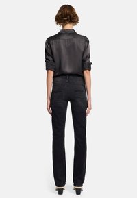 Svarta jeans med rak bendesign, bakfickor med kurviga detaljer, kombinerat med en mörk satinskjorta som har uppvikt ärmar.