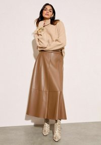 Beige kudumü turtleneck-sweater, millel on lõtv lõige ja volditud varrukad, koos pruunist kunstnahast seeliku, mis on flared siluetiga ja sujuva disainiga.