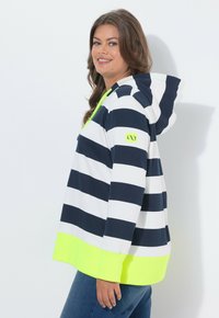 Sudadera con capucha a rayas en azul marino y blanco, con un dobladillo y detalles en amarillo neón brillante. Confeccionada con tela ligera y un corte relajado.