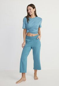 Teal lounge set met een geknoopte top met korte mouwen en een korte broek. Zachte stof met een relaxte pasvorm en een zakdetails op de broek.