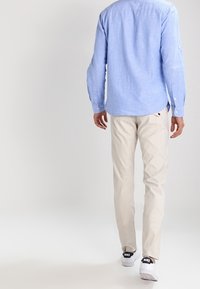Camicia azzurra a maniche lunghe, pantaloni beige e sneakers neri di marca. La camicia presenta un colletto con bottoni e un orlo arrotondato.