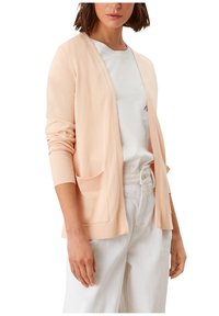 Jasnopomarańczowy kardigan z prążkowanymi rękawami i dołem, z dwoma przednimi kieszeniami i otwartym krojem. Noszony na białej koszulce i jasnych spodniach.