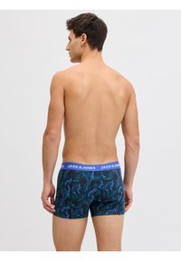 Άνδρας που είναι γυρισμένος με την πλάτη φοράει μαύρα μπόξερ με σχέδιο μπλε και πράσινα φύλλα και μπλε μέση με ετικέτα "JACK & JONES" σε λευκό φόντο.