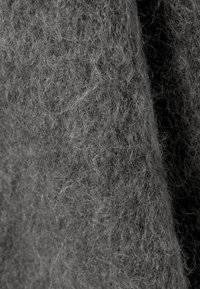 Textil din lână gri, cu o textură moale și pufos, având fibre fine. Suprafața pare densă și ușor haotică, sugerând căldură și confort.
