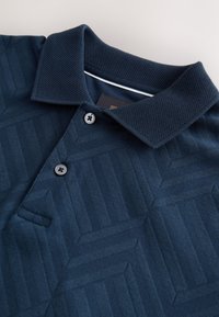 Marineblaues Poloshirt mit strukturiertem geometrischem Muster, zwei Knöpfen und einem dezenten weißen Besatz innen am Kragen.