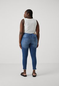 Skinny jeans in medium blue denim with a high waist, featuring a frayed hem and back pockets. Paired with a white ribbed tank top.