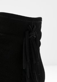 Černé semišové kotníkové boty s třásněmi a prošívaným okrajem. Materiál se jeví jako měkký s matným povrchem, což zvýrazňuje texturu.