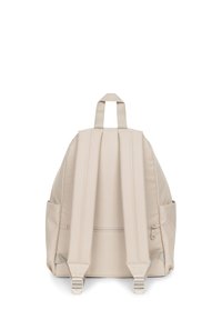 Mochila de tela beige con correas acolchadas para los hombros, asa superior, bolsillos laterales y compartimento principal con cremallera. Textura suave y diseño minimalista.