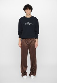 Námořnická mikina s bílou vyšívanou nášivkou, doplněná o lesklé hnědé kalhoty s širokými nohavicemi a bílé tenisky. Pohodový outfit s volným střihem.