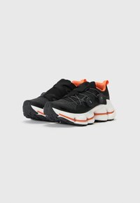 Schwarze Sportschuhe mit orangen Akzenten, Mesh-Obermaterial und klobigem weißen Zwischensohle. Verfügt über ein Schnürsystem und Gummisohle für Griffigkeit.