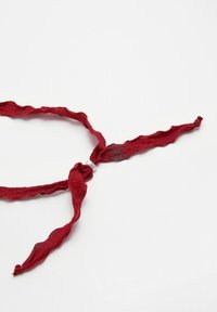 Röd strukturerad band med en vågig kant, knuten i en knut och avslutad med en liten vit pärla som accent.
