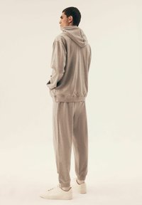 Szary dres składający się z bluzy z kapturem i spodni dresowych, wykonany z bawełnianego materiału, o luźnym kroju, z prążkowanymi mankietami i pasem, zestawiony z białymi sneakersami.