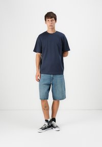 Marineblauses T-Shirt mit kurzen Ärmeln kombiniert mit hellblauen Denim-Shorts, dazu hohe schwarze Sneakers mit weißen Akzenten. Einfaches Design.