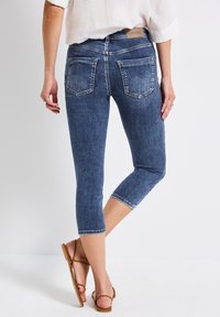 Pantalons capri en jean de couleur bleu foncé, avec une coupe ajustée, des poches arrière et des ourlets surpiqués, associés à des sandales à lanières de couleur marron clair.