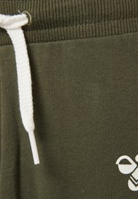 Olivgröna sweatpants har en ribbad midja med ett vitt snöre och en liten vit grafisk detalj på den nedre sidan.