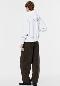 Szürke, rövidített kapucnis pulóver, húzózsinórral, laza, mintás barna nadrággal, amely bonyolult mintákkal díszített. Fekete lábbeli teljesíti a megjelenést.