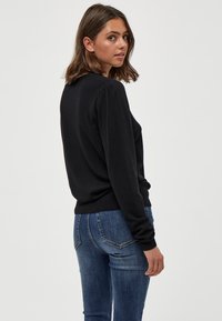 Pullover nero con un design aderente, polsini a costine e tessuto testurizzato. Abbinato a jeans in denim blu con tasche posteriori.