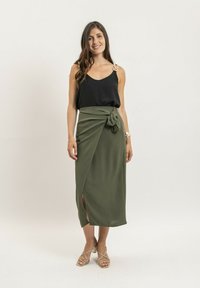 Top noir sans manches avec des bretelles décoratives, associé à une jupe portefeuille olive à mi-mollet avec une lanière sur le côté et une fente.