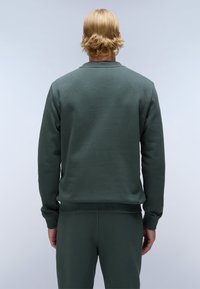 Donkergroene sweatshirt van fleece stof. Heeft een ronde halslijn, ribgebreide manchetten en zoom, met een gladde textuur en een relaxte pasvorm.
