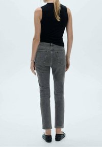 Czarny bezrękawnik, szare jeansy o wysokim stanie z tylnymi kieszeniami, dopasowane, proste nogawki, średni stan, noszone z czarnymi baletkami.