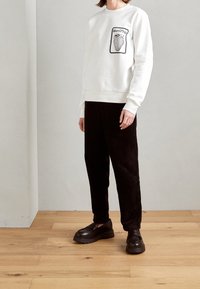 Vit sweatshirt med jordgubbsgrafik på framsidan, kombinerad med svarta kordflöjtsbyxor och kraftiga svarta loafers. Slät tyg, avslappnad passform.