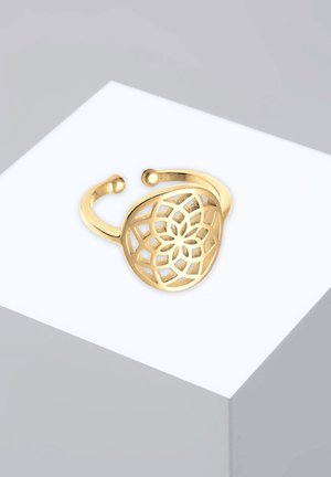 Anello in tonalità oro con un design floreale a intaglio, caratterizzato da una fascia divisa e estremità arrotondate. Realizzato in metallo, presenta un intricato gioco geometrico.