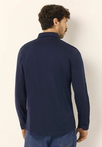 Camicia a maniche lunghe blu navy con colletto, polsini con bottone e una texture liscia. Presenta un colore uniforme e una vestibilità comoda.
