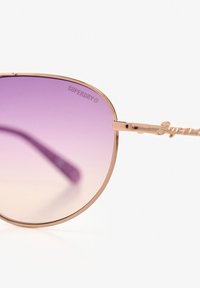 Ronde zonnebrillen met een roségouden metalen frame, paarse gradientlenzen en geprofileerde armen met de merknaam "Superdry."