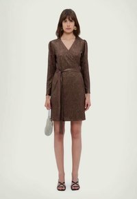 Hnedé metalické šaty s dlhými rukávmi a viazaným pásom. Majú hladkú textúru a siahajú po kolená. Doplnkom sú malé kabelky.