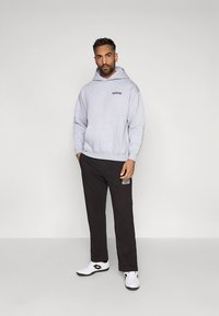 Sweat à capuche gris avec poche avant et petit logo, associé à un pantalon noir avec logo, et des chaussures de sport blanches.