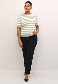 Stribet strikbluse i beige og hvid, kort ærme, rund halsudskæring. Sammen med sorte slim-fit jeans og sorte spidse stilletter.