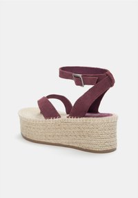 Burgundy mockasinsandaler med plattform och korskorsade remmar samt en vävd jute-mellansula. Har en spännsrem vid ankeln för en säker passform.