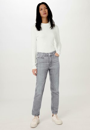 Witte langemouwige top gecombineerd met lichtgrijze, high-waisted jeans met een rechte pasvorm en een subtiele vervaagde patroon, gedragen met beige sneakers.