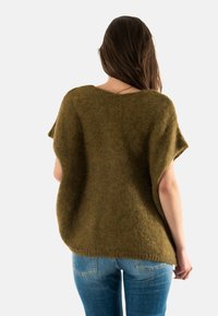 Suéter de punto de color verde oliva, de gran tamaño y de manga corta, con un cuello barco ancho. Textura suave y corte ligeramente holgado. Combinado con jeans de mezclilla azul.